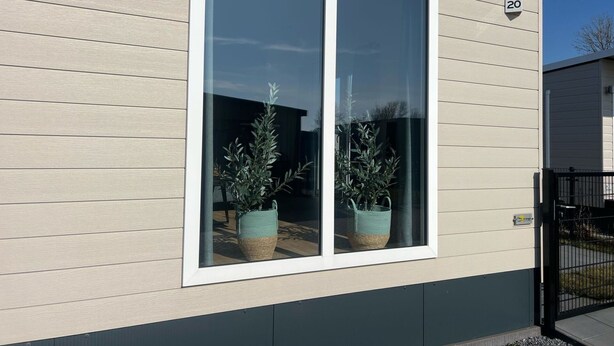 Ein modernes Gebäude mit einem großen Fenster, einem Schild mit der Nummer 20 und zwei Kübelpflanzen davor.