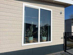 Een modern gebouw met een groot raam, een bord met het nummer '20' en twee planten in potten voor de gevel.