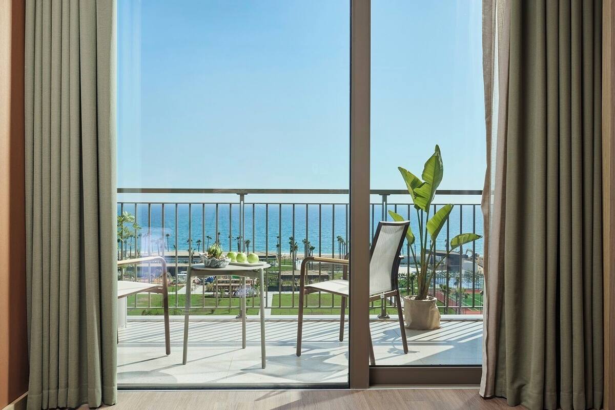 A balcony with a view of the sea, a table with plants, and a chair.