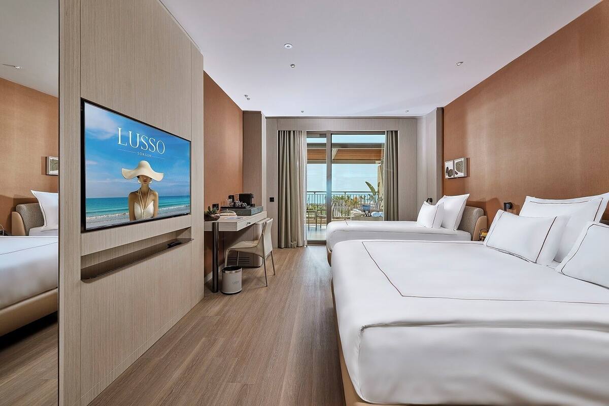 A hotel room with a large TV, a desk, two beds, and a balcony with a view of the ocean.