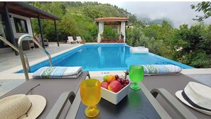 Relax by the serene pool surrounded by lush greenery and hills.