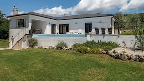 A modern two-story house with a swimming pool, a covered patio, and a stone retaining wall.