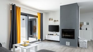 A modern living room with a grey sofa, a flat-screen TV, a fireplace, and a balcony with yellow curtains.