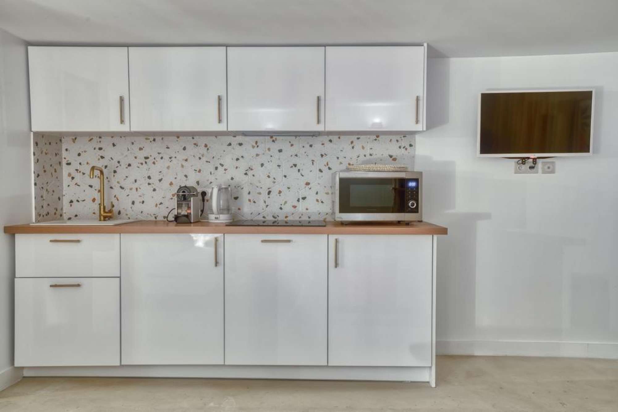 A compact kitchen with white cabinets, a microwave, a coffee maker, and a small sink.