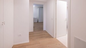 Un corridoio con pareti bianche e pavimento in legno, che conduce a una stanza con una porta bianca.