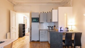 A compact kitchen with white cabinets, a small dining area with two chairs, and a wooden floor. - Central 1BR Quai de Seine in the Marais district (Paris)
