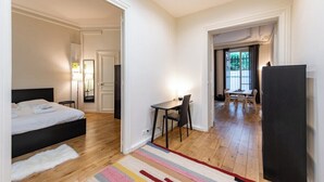 A bedroom with a bed, bedside table, and lamp. There is a hallway leading to a dining area with a table and chairs. - Central 1BR Quai de Seine in the Marais district (Paris)