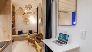 Una habitación moderna y luminosa con un escritorio blanco, una computadora portátil y un área de descanso confortable con cojines y una pequeña mesa.