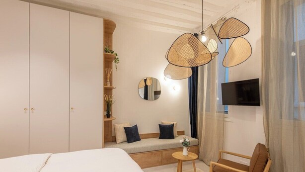 Un dormitorio moderno con una cama grande, un sofá, una mesita y un televisor montado en la pared.