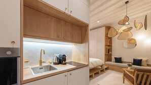 Cocina moderna con armarios de madera, un lavamanos y una cafetera. Hay una zona de estar con un sofá y una mesa.