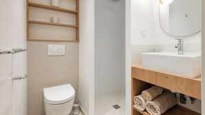 Un baño moderno con inodoro, ducha y tocador con espejo y lavamanos.