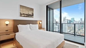 Une chambre d’hôtel moderne avec un grand lit, une vue sur la ville, un tableau encadré au mur et une table de chevet avec une lampe.
