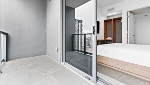 Une chambre d’hôtel moderne avec balcon, un lit et une vue sur le paysage urbain.