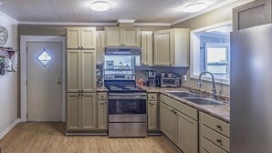 A kitchen with light-colored cabinets, stainless steel appliances, and a window providing natural light. - Cocodrie Waterfront Fishing Camp - Sportsmans Paradise (Chauvin)