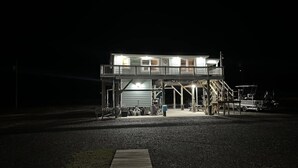 A two-story building with a balcony and a covered area with a vehicle parked inside. - Cocodrie Waterfront Fishing Camp - Sportsmans Paradise (Chauvin)