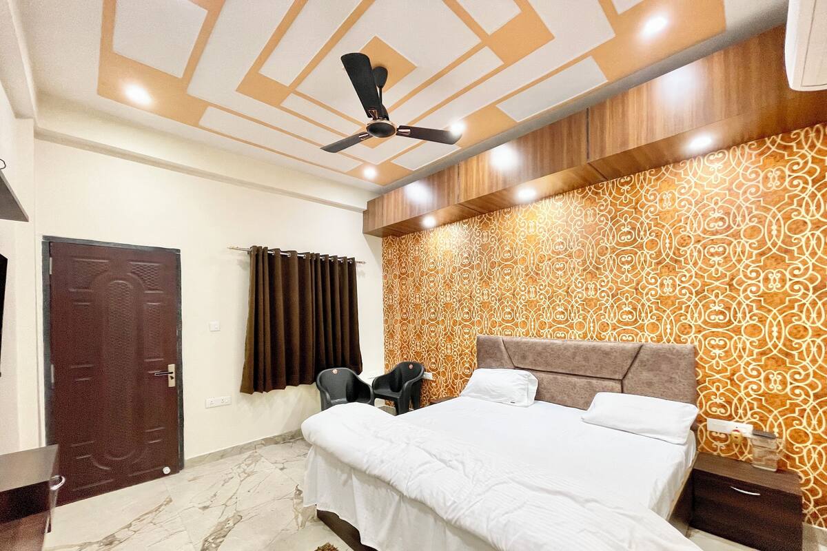 A hotel room with a bed, a ceiling fan, a patterned wall, a door, and a nightstand.