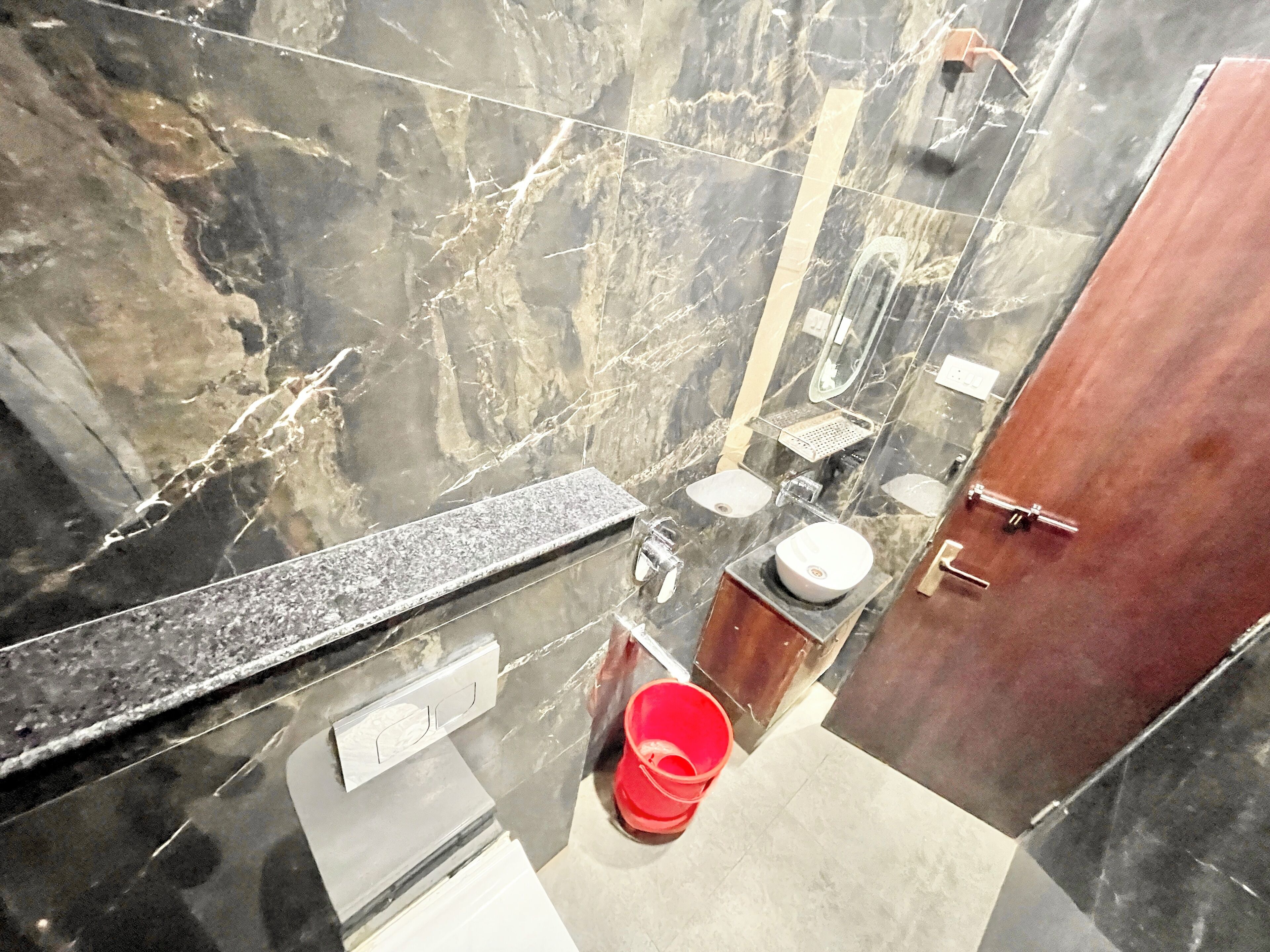 Ein Badezimmer mit Marmorwaschtisch, einem Waschbecken, einem Spiegel und einem roten Eimer.
