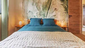 Ein Schlafzimmer mit einem großen Bett, einem Holzschrank und einer Wand mit tropischen Blattmotiven.