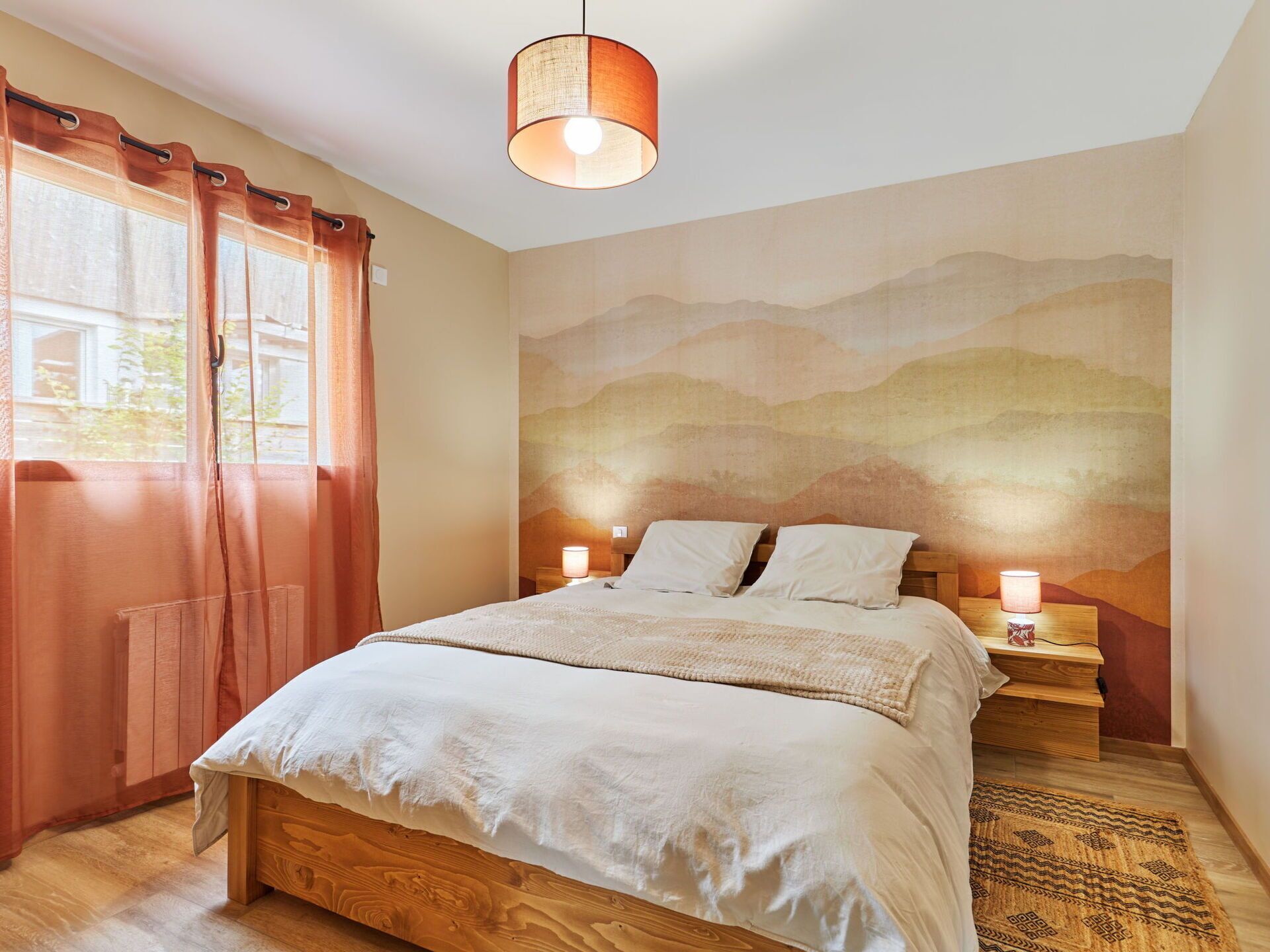 A bedroom with a wooden bed, two bedside lamps, a window with curtains, and a wall mural.