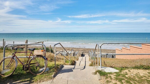 Ein Weg führt zu einem Strand, links steht ein Fahrrad.