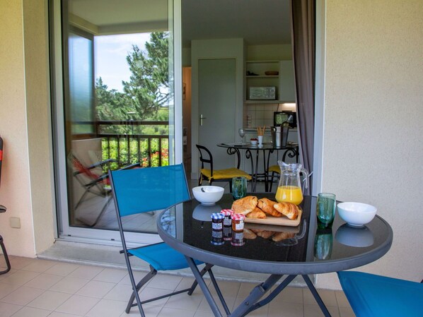 Un balcon avec une table préparée pour le petit-déjeuner, comprenant des croissants, un pichet de jus d’orange et des pots de confiture.