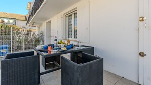 A balcony with a table set for dining, wicker chairs, and a white door. - Beautiful apartment for 4 people with A/C, WIFI, TV, terrace and pets allowed (Le Grau-du-roi)