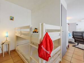 Kerrossängyllä varustettu huone, jossa on pieni työpöytä, lamppu ja punainen laukku, joka on ripustettu kerrossängyn yläosaan.