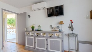 A room with a grey cabinet displaying seashells, a mounted TV, and decorative items including a rooster and a lamp. - Beautiful apartment for 4 people with A/C, WIFI, TV, terrace and pets allowed (Le Grau-du-roi)