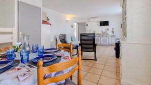 A dining area with a table set for four, a sofa, and a TV in the background. - Beautiful apartment for 4 people with A/C, WIFI, TV, terrace and pets allowed (Le Grau-du-roi)