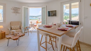 Un comedor con mesa de madera, sillas blancas y vistas al mar a través de puertas abiertas.