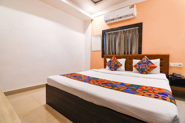 Un lit bien fait, agrémenté d’un couvre-lit aux motifs géométriques colorés, une tête de lit ornée de coussins décoratifs et un climatiseur fixé au mur.