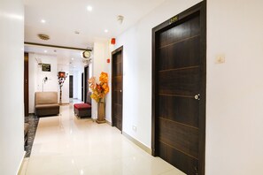 A hotel hallway with a dark wooden door labeled "503", a beige armchair, a red ottoman, and a vase with orange flowers. - Fabhotel Gr Hospitality (Barasat)