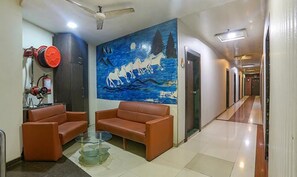 Eine Lobby mit Wandgemälde, zwei braunen Sofas, einem Glastisch und einem Deckenventilator.