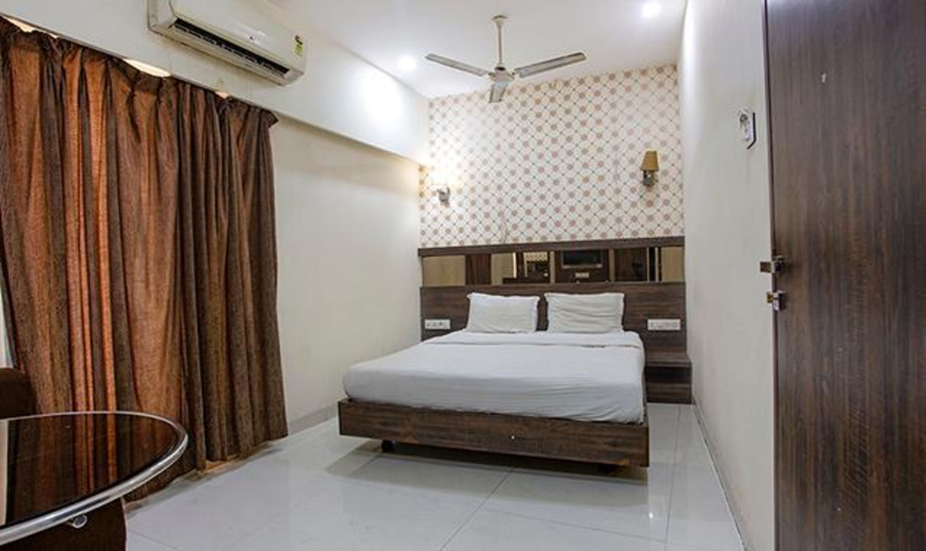A bedroom with a bed, curtains, an air conditioner, a ceiling fan, and a wooden door.