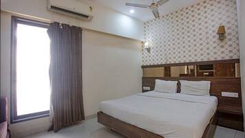 A hotel room with a large bed, a ceiling fan, an air conditioning unit, a window with curtains, and a patterned wall.