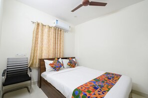 Un dormitorio con una cama, una silla, un ventilador de techo y un equipo de aire acondicionado.