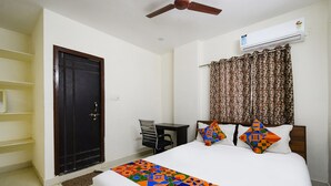 A hotel room with a bed, a desk, a chair, a wardrobe, and an air conditioning unit.
