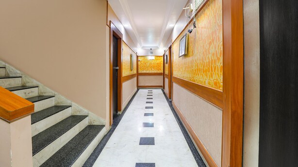 A long, narrow hallway with a marble floor, wooden paneling on the walls, and a staircase on the left. - Fabhotel Apple Inn (Ahmedabad)