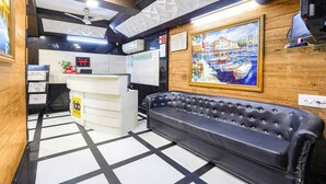 A hotel lobby with a black leather sofa, a reception desk, a painting of a harbor, and a digital clock. - Fabhotel Apple Inn (Ahmedabad)