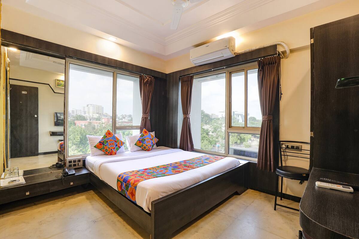 A modern hotel room with a large bed, a desk with a chair, a TV, and a window with curtains.