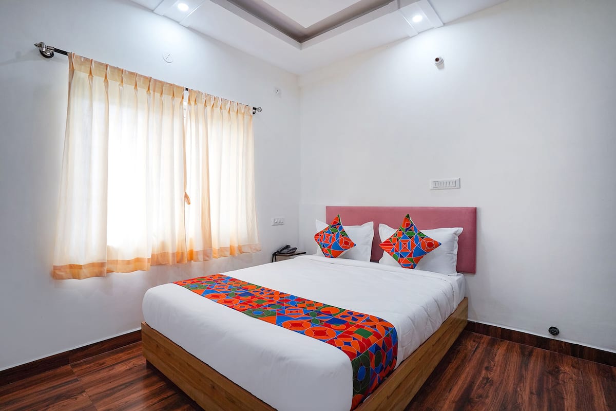 A neatly made bed with a colorful bedspread, a wooden headboard, and a window with sheer curtains.