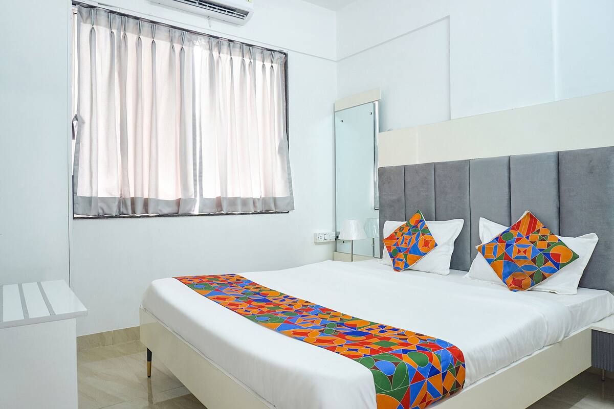 A hotel room with a bed, a window with curtains, a bedside table, and a nightstand with a lamp.
