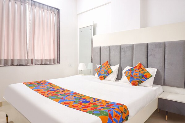 Une chambre d’hôtel moderne avec un grand lit, une tête de lit grise et un plaid coloré.