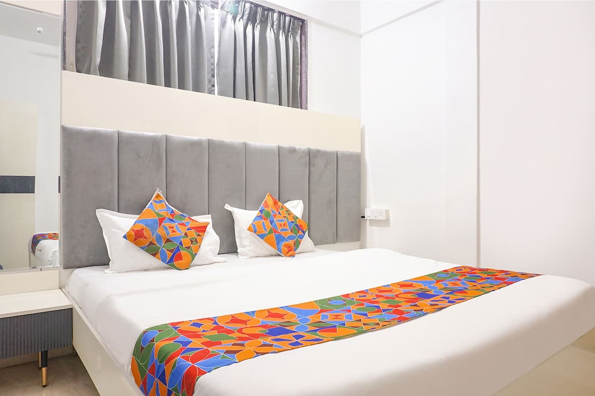 A hotel room with a large bed, grey headboard, white bedding, and colorful throw pillows.