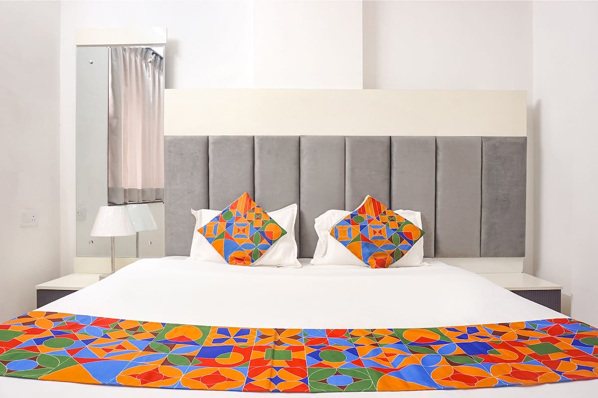A hotel room with a bed, a nightstand, a lamp, and a window with a curtain.