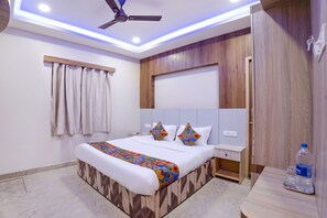 A modern bedroom with a bed, ceiling fan, bedside table, and a water bottle on a nightstand. - Fabhotel Wooden Park (Chennai)