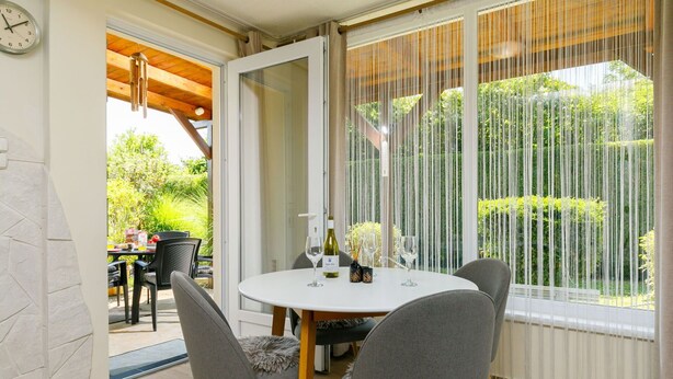 Un comedor con una mesa redonda, cuatro sillas y vistas a un jardín a través de ventanas amplias con cortinas ligeras.