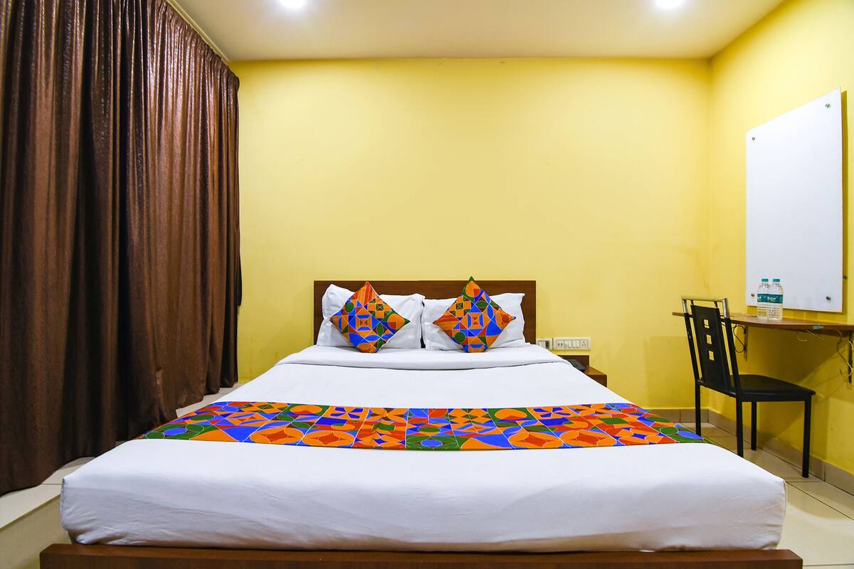 A hotel room with a bed, a chair, a desk with a computer, and a whiteboard.