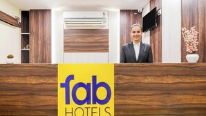 Un comptoir d’accueil avec un revêtement en bois, un téléviseur à écran plat fixé au mur et une enseigne indiquant « fab hotels ».