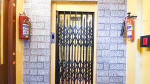 Une porte munie d’une grille de sécurité en métal, des extincteurs fixés au mur et un mur recouvert de carreaux.